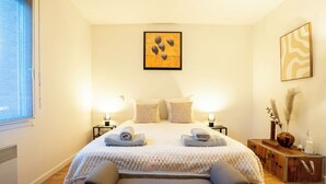 A neatly arranged bedroom with a bed, bedside lamps, a bench, and artwork on the walls. - Cosy air-conditioned T3 with exterior -Toulouse est (Toulouse)