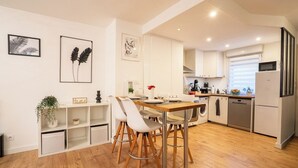 A modern kitchen with white cabinets, a dining table with chairs, and a built-in washing machine. - Cosy air-conditioned T3 with exterior -Toulouse est (Toulouse)
