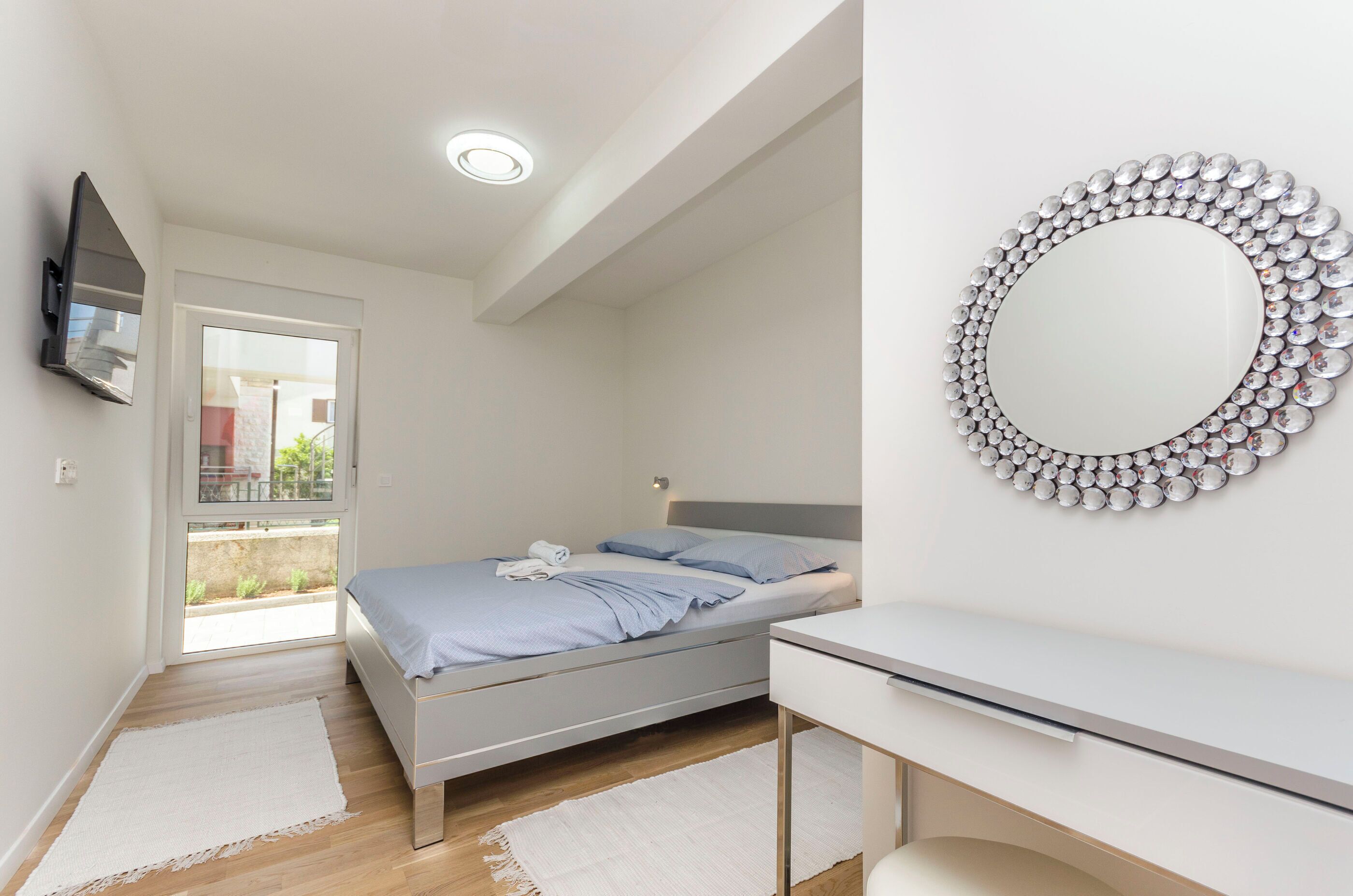A modern bedroom with a bed, a bedside table, a mirror with a decorative frame, and a television mounted on the wall.