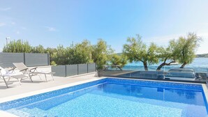 A swimming pool with clear blue water, surrounded by lounge chairs and a view of the sea. - Apartment Adriatic With Pool (Vodice)