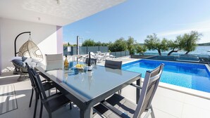 A modern outdoor dining area with a glass table, black chairs, and a hanging chair. - Apartment Adriatic With Pool (Vodice)