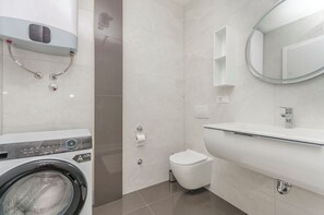 A modern bathroom with a built-in washing machine, a toilet, and a large mirror. - Apartment Adriatic With Pool (Vodice)