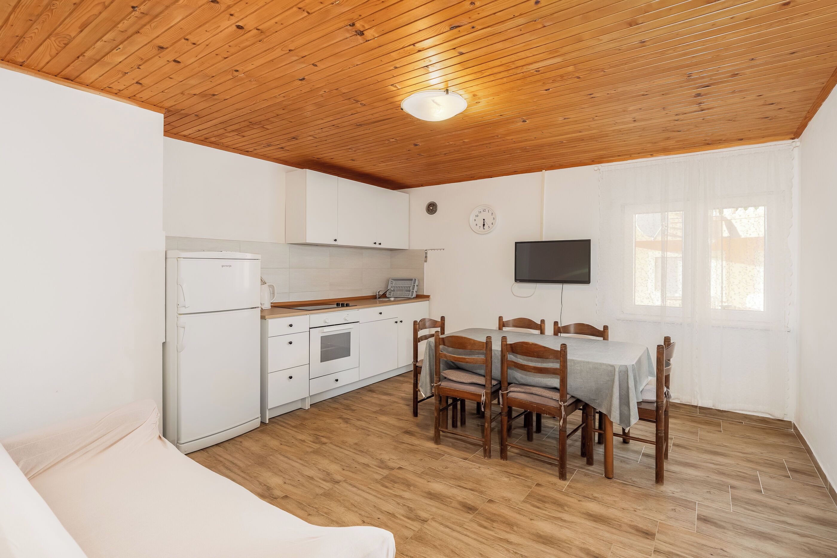 A compact kitchen with white cabinets, a built-in oven, and a dining area with wooden chairs and a table.