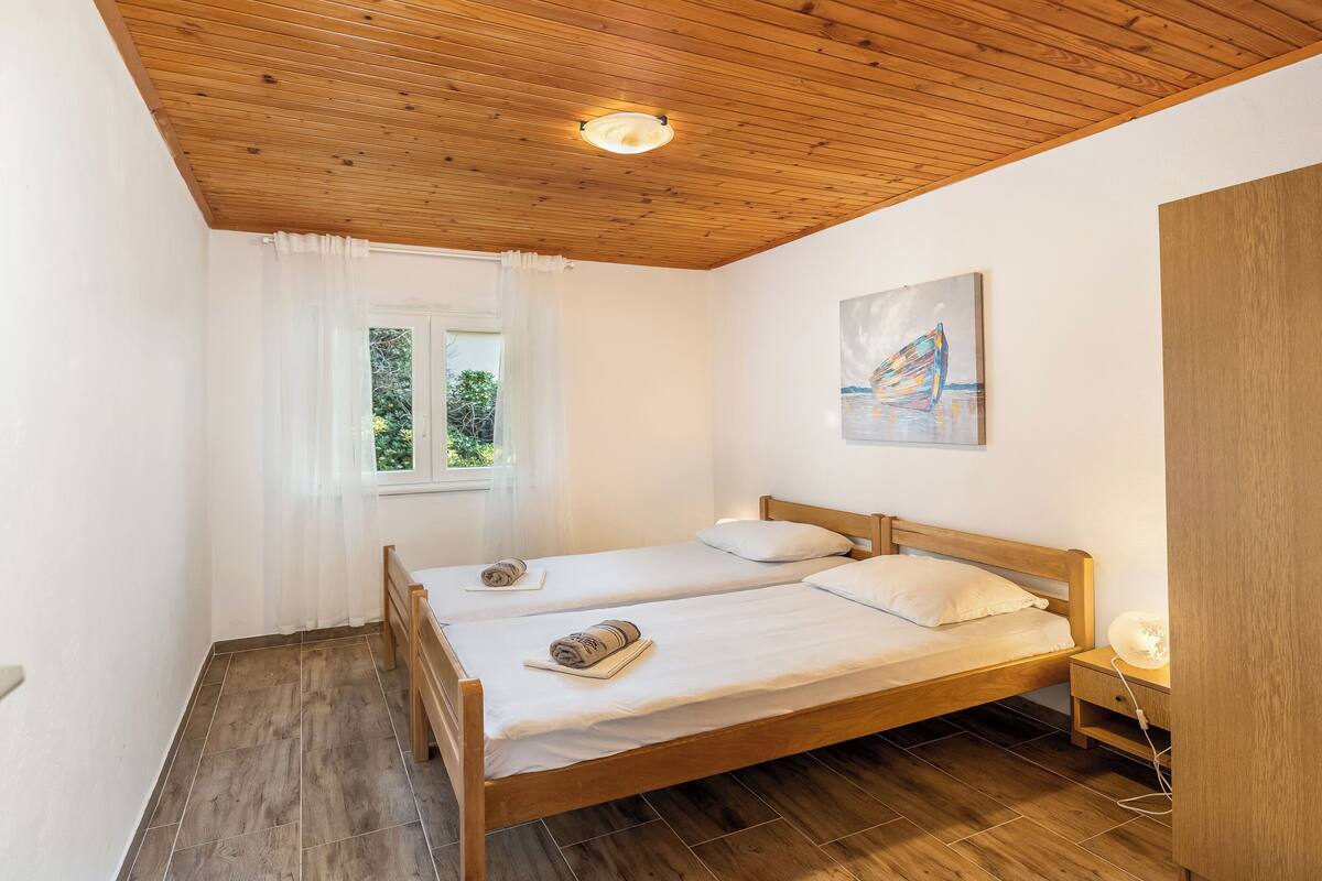 Une chambre avec deux lits en bois, une fenêtre avec des rideaux blancs, un tableau au mur et un plafond en bois.