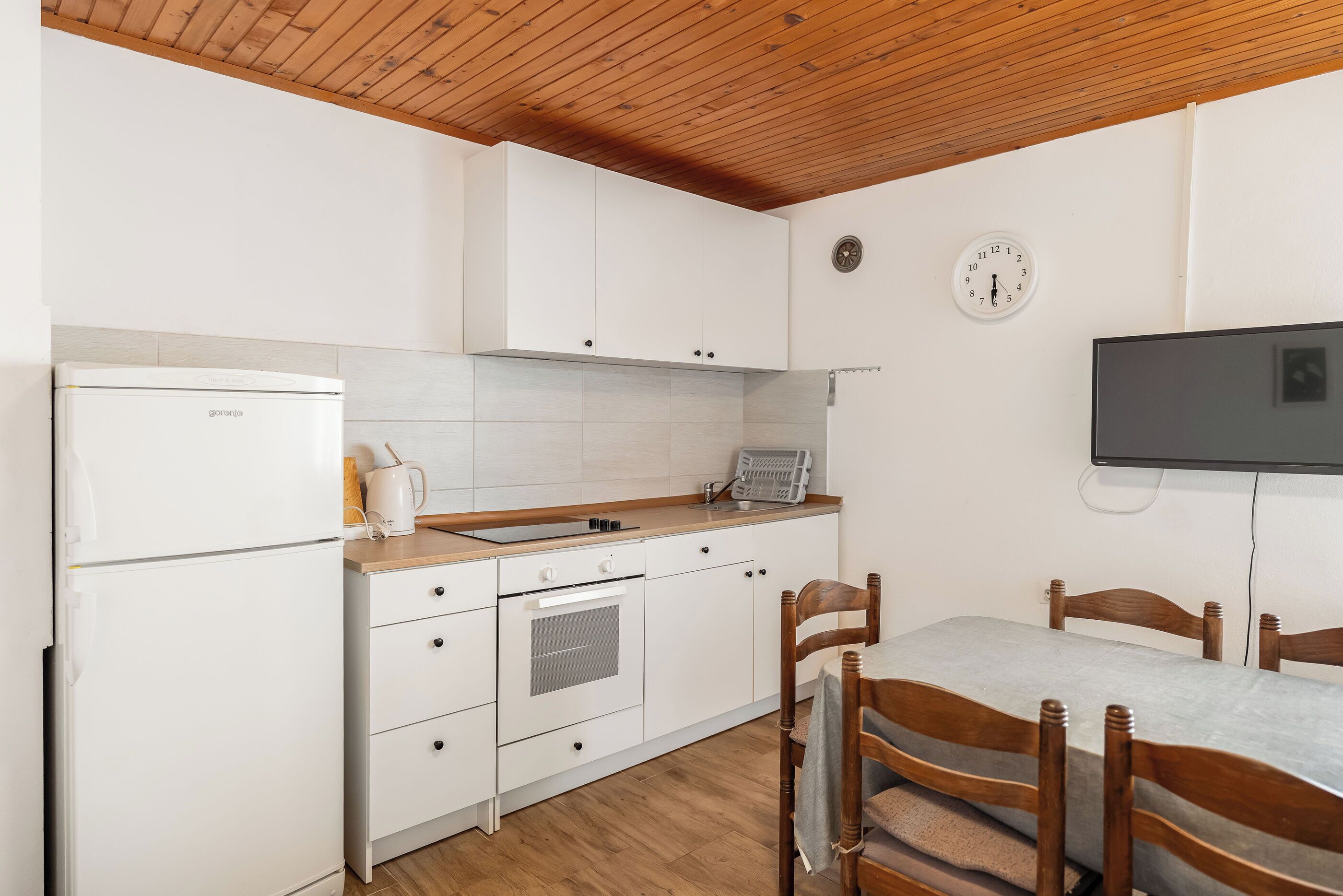 A compact kitchen with white cabinets, a built-in oven, a sink, and a wooden ceiling.
