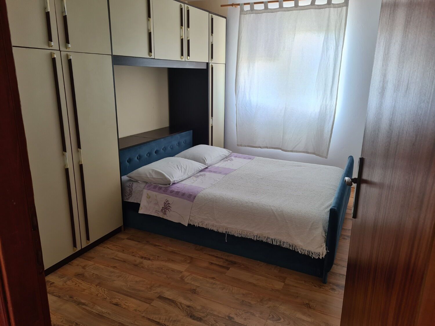 A bedroom with a bed, a wardrobe, and a window with curtains.