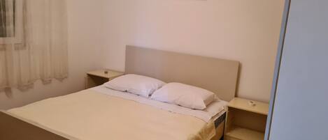 A neatly arranged bedroom with a bed, two bedside tables, a window with curtains, and a painting on the wall.
