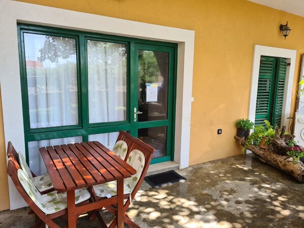A wooden table and chairs set outside a building with green shutters and a yellow wall. - Apartments Stosa (Nin)