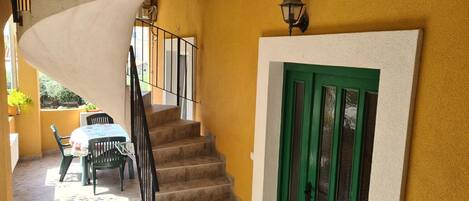 A staircase leading to a room with a green door, a table with chairs, and a view of the outside.