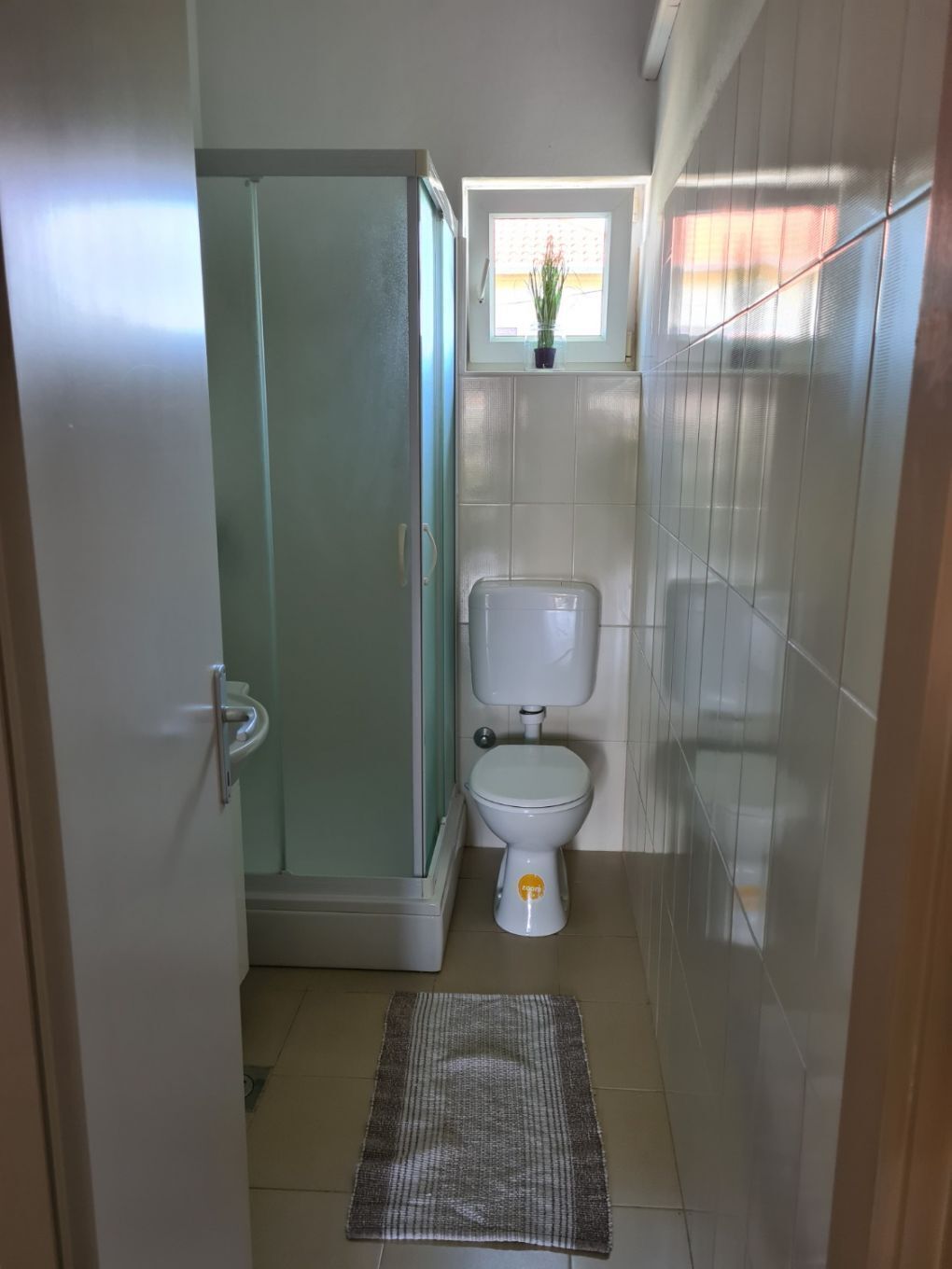 A small bathroom with a toilet, a glass shower enclosure, and a window above the toilet.