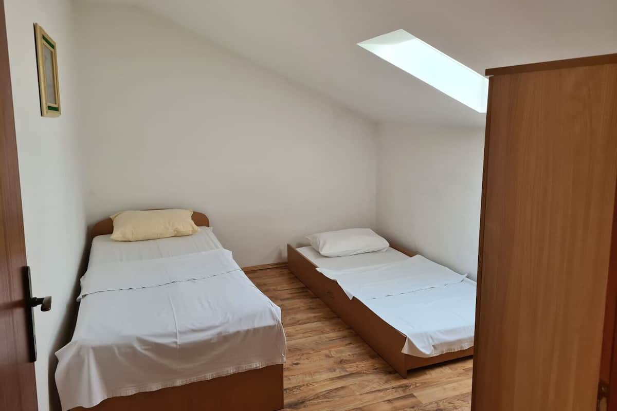 A small, single-room accommodation with two beds, a skylight, and a wooden floor.