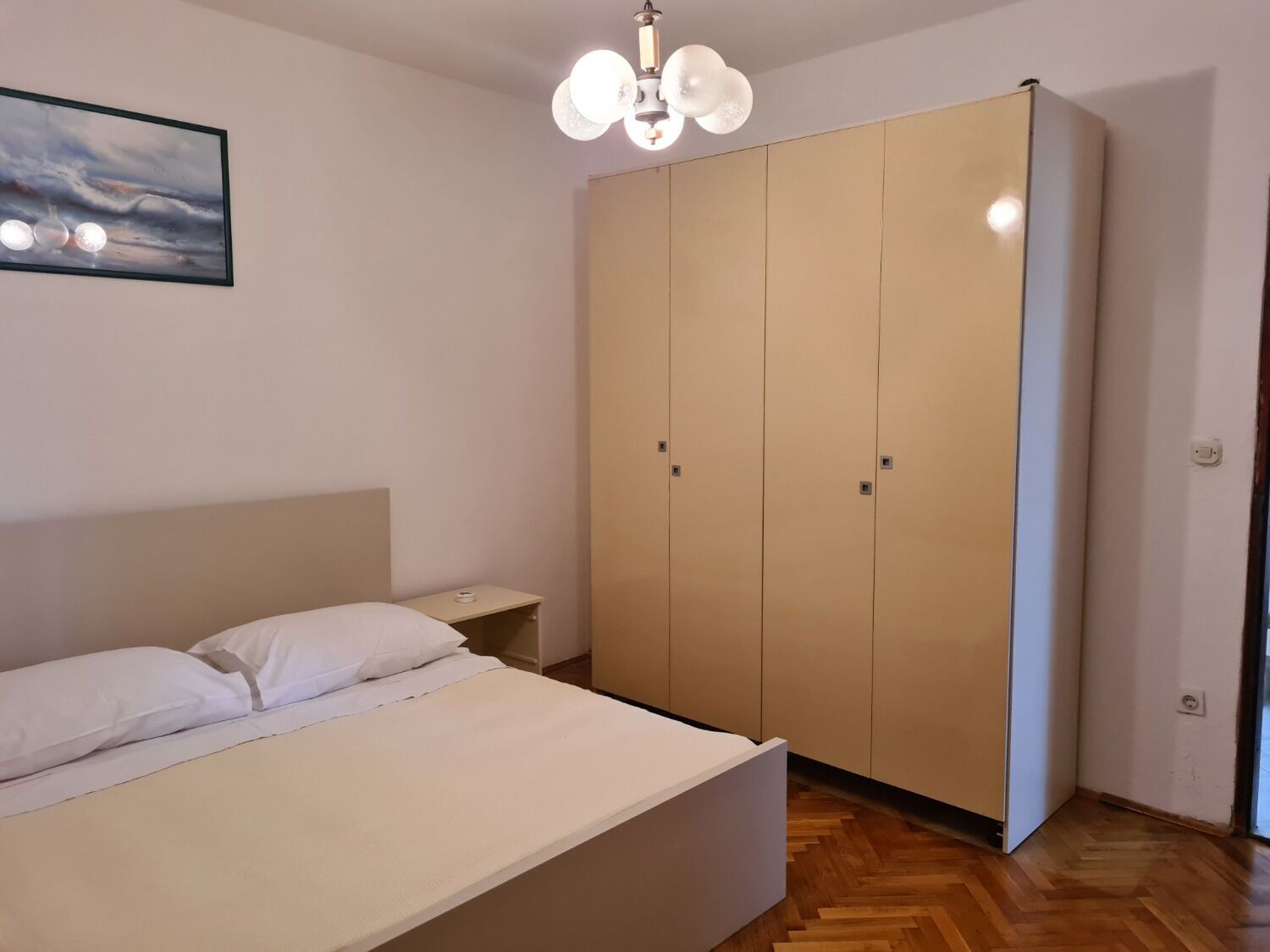 A bedroom with a bed, a wardrobe, a nightstand, and a ceiling light fixture.