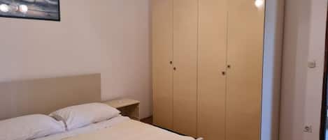 A bedroom with a bed, a wardrobe, a nightstand, and a ceiling light fixture.