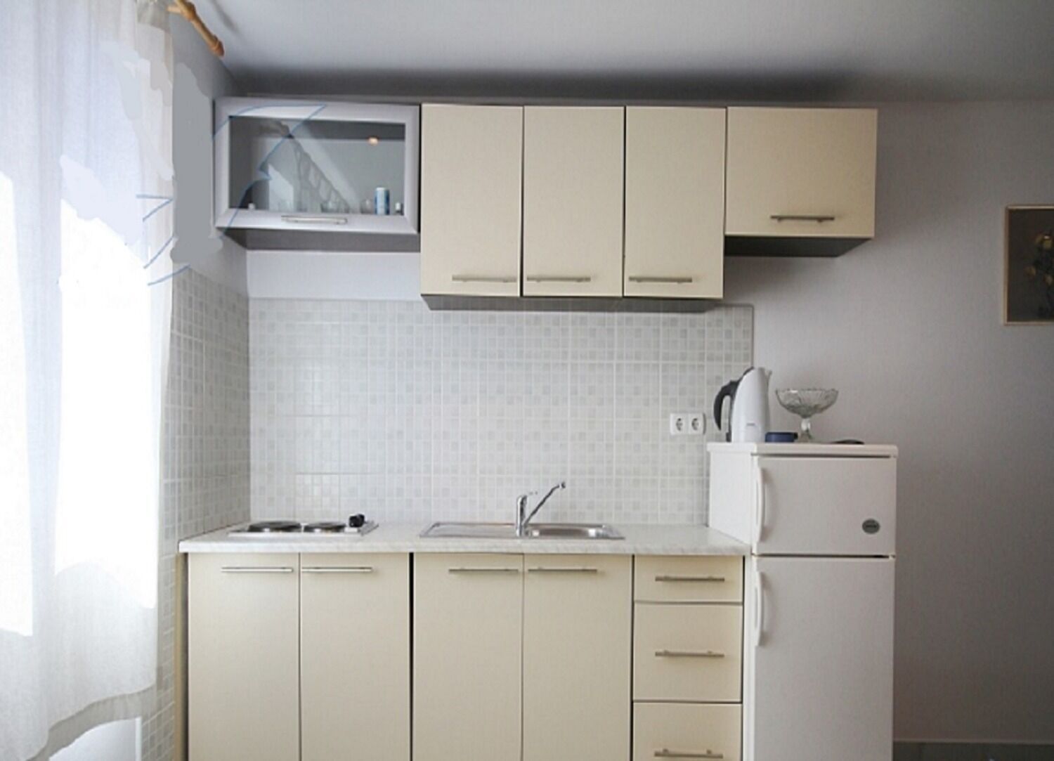 Een compacte keuken met lichte kastjes, een ingebouwde magnetron en een kleine koelkast.