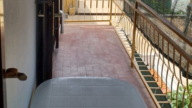 Un balcón con vistas a un pueblo costero, barandilla metálica y una puerta que da al interior.