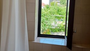 Un baño con ventana, cortina de ducha y vistas a una casa y follaje exterior.