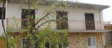A two-story house with a balcony, stone facade, and a tree in the foreground.