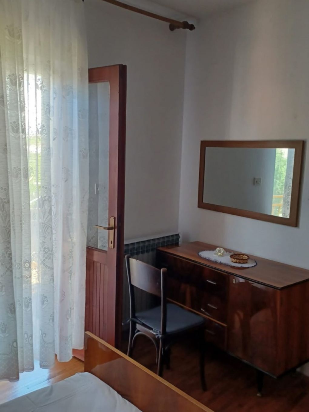 Ein Zimmer mit einem Holztisch, einem Stuhl, einem Bett und einem Spiegel an der Wand.