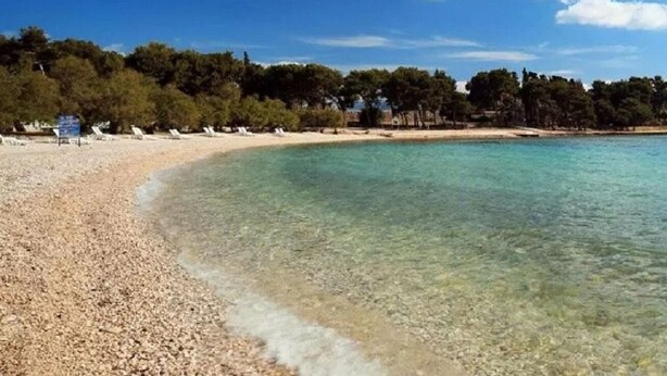 A beach with clear turquoise water, pebbly shore, and a row of white lounge chairs. - Apartments Brti (Supetar)
