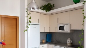 Une cuisine compacte équipée d’un réfrigérateur, d’un four à micro-ondes et d’un lave-linge. On y trouve une table à manger avec des chaises et un canapé.