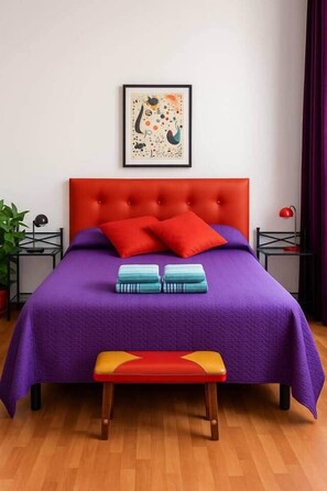A bed with a red headboard, purple bedding, and two red pillows. There is a framed artwork above the bed and a bench in front of it. - Ole Málaga - Superior (Malaga)