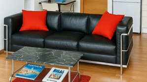 Un salon moderne avec un canapé en cuir noir, des coussins rouges, une table basse en marbre et un tapis rouge.
