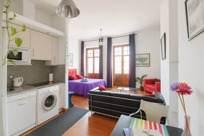 A compact living space with a kitchenette, a bed with purple bedding, a red sofa, and a dining area with a table and chairs. - Ole Málaga - Superior (Malaga)