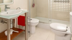 Une salle de bain moderne avec une douche à parois de verre, deux toilettes, un lavabo et un grand miroir.