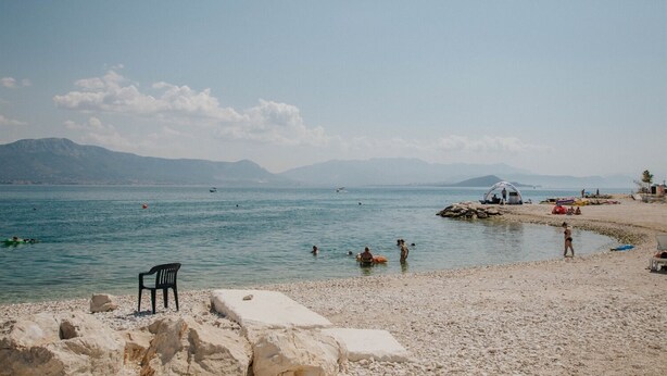 A beach with a rocky shoreline, a few people swimming, and a tent set up on the sand. - Apartments Dome (Trogir)