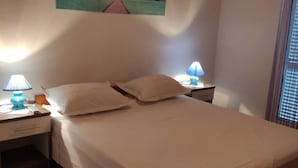 A bedroom with a single bed, two bedside tables with lamps, a painting on the wall, and a window with blinds. - Apartments Andelka (Marina)