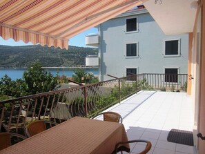 An outdoor terrace with a table and chairs, a view of a body of water, and a building with balconies. - Apartments Andelka (Marina)