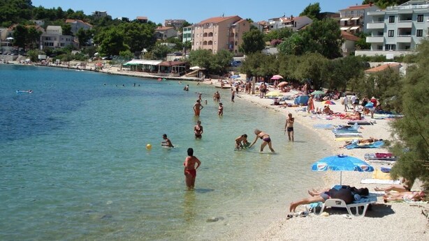 A beach with clear water, people swimming and sunbathing, and buildings in the background. - Apartments Andelka (Marina)