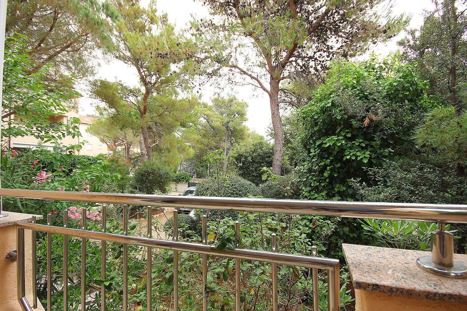 A balcony with a metal railing overlooking a garden with various trees and shrubs.