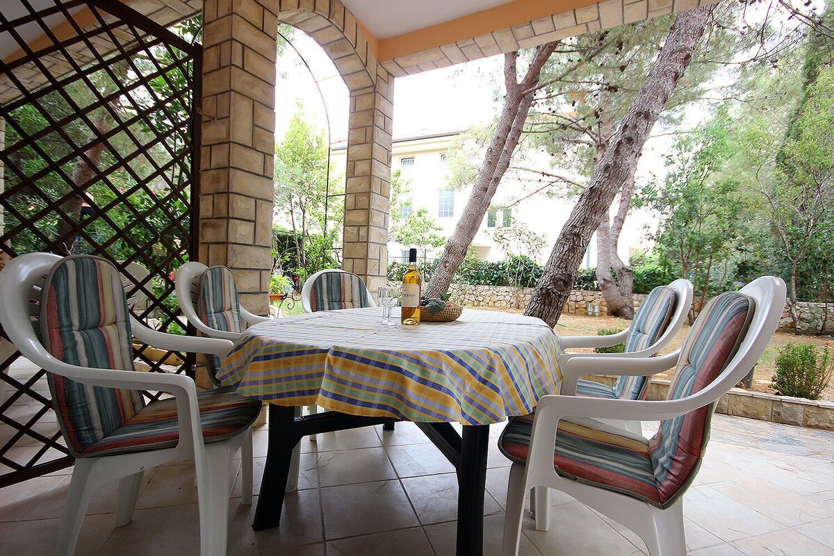 A patio with a round table and six chairs, surrounded by a stone wall and trees.