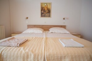 A double bed with two pillows, a wooden headboard, and a painting above. - Apartments and Rooms Ivan (Novalja)