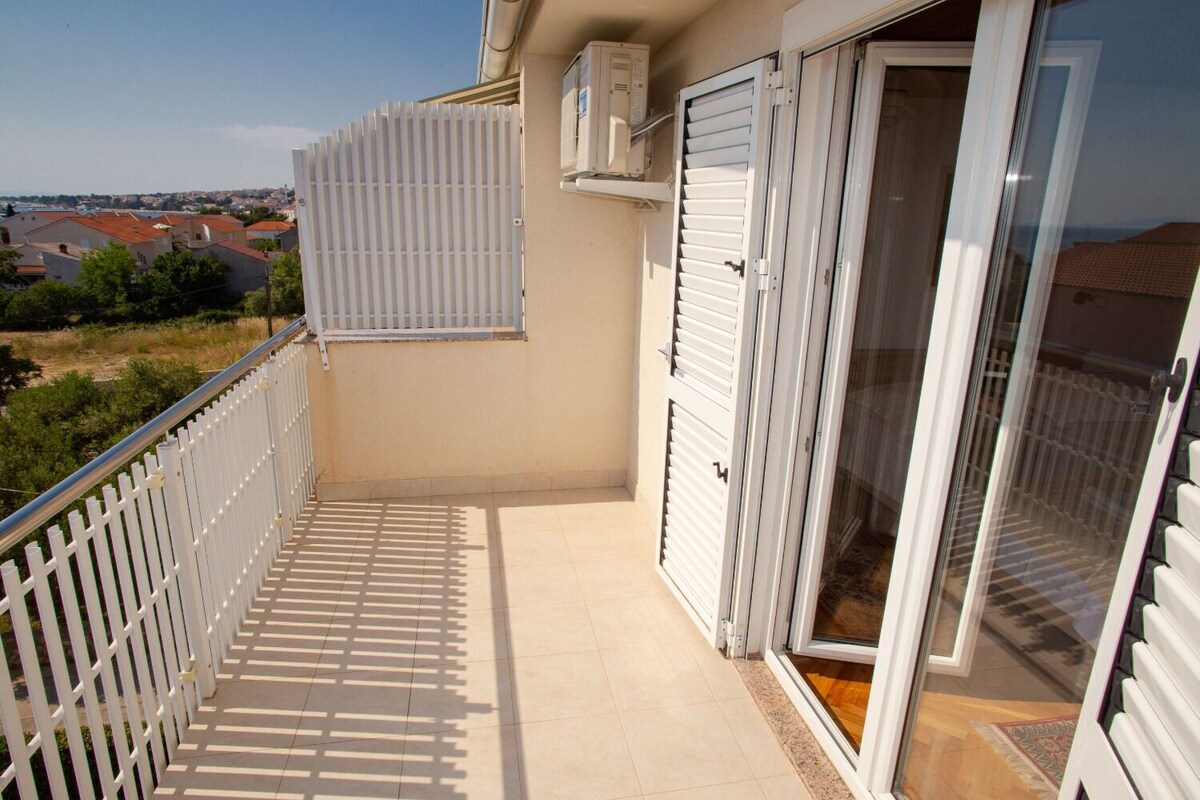 A balcony with a white railing, a sliding glass door, and a view of a residential area.