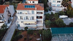 A multi-story residential building with a red-tiled roof, balconies, and a small garden area. - Apartments and Rooms Ivan (Novalja)