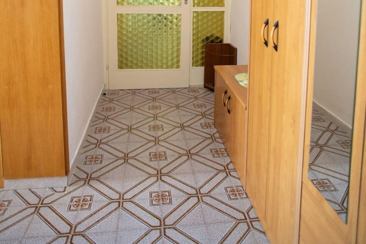 A hallway with patterned floor tiles, a wooden wardrobe, and a door with frosted glass panels.