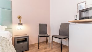 Une chambre avec un lit, une table de chevet, une lampe fixée au mur, deux chaises, un réfrigérateur blanc et un four à micro-ondes posé sur une étagère en bois.