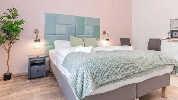 Une chambre à coucher moderne avec un grand lit, une table de chevet, une plante en pot et un petit bureau avec un ordinateur.