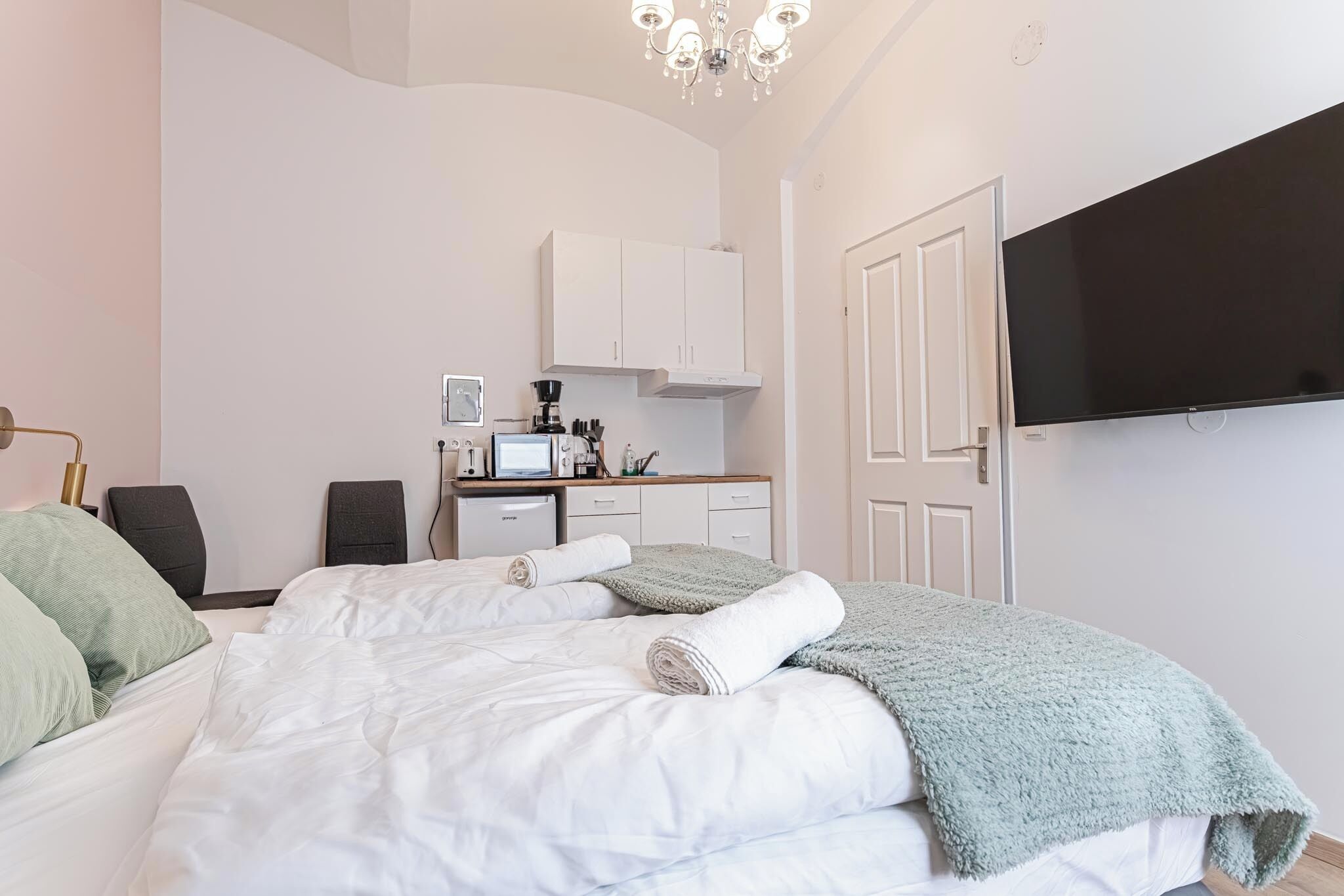 A bedroom with a bed, a TV, a desk, and a kitchenette.