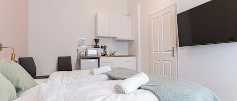 A bedroom with a bed, a TV, a desk, and a kitchenette.