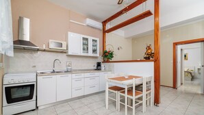 A kitchen with white cabinets, a microwave, a stove, and a dining table with chairs. - Apartments Mig (Rab)