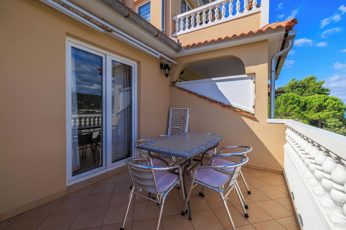 Un balcon avec une table et des chaises, une porte-fenêtre coulissante et une vue sur la verdure.