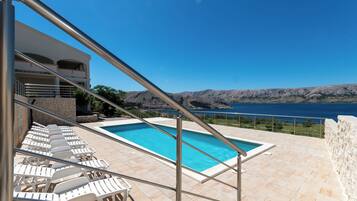A pool with lounge chairs, a stone wall, and a view of the sea.