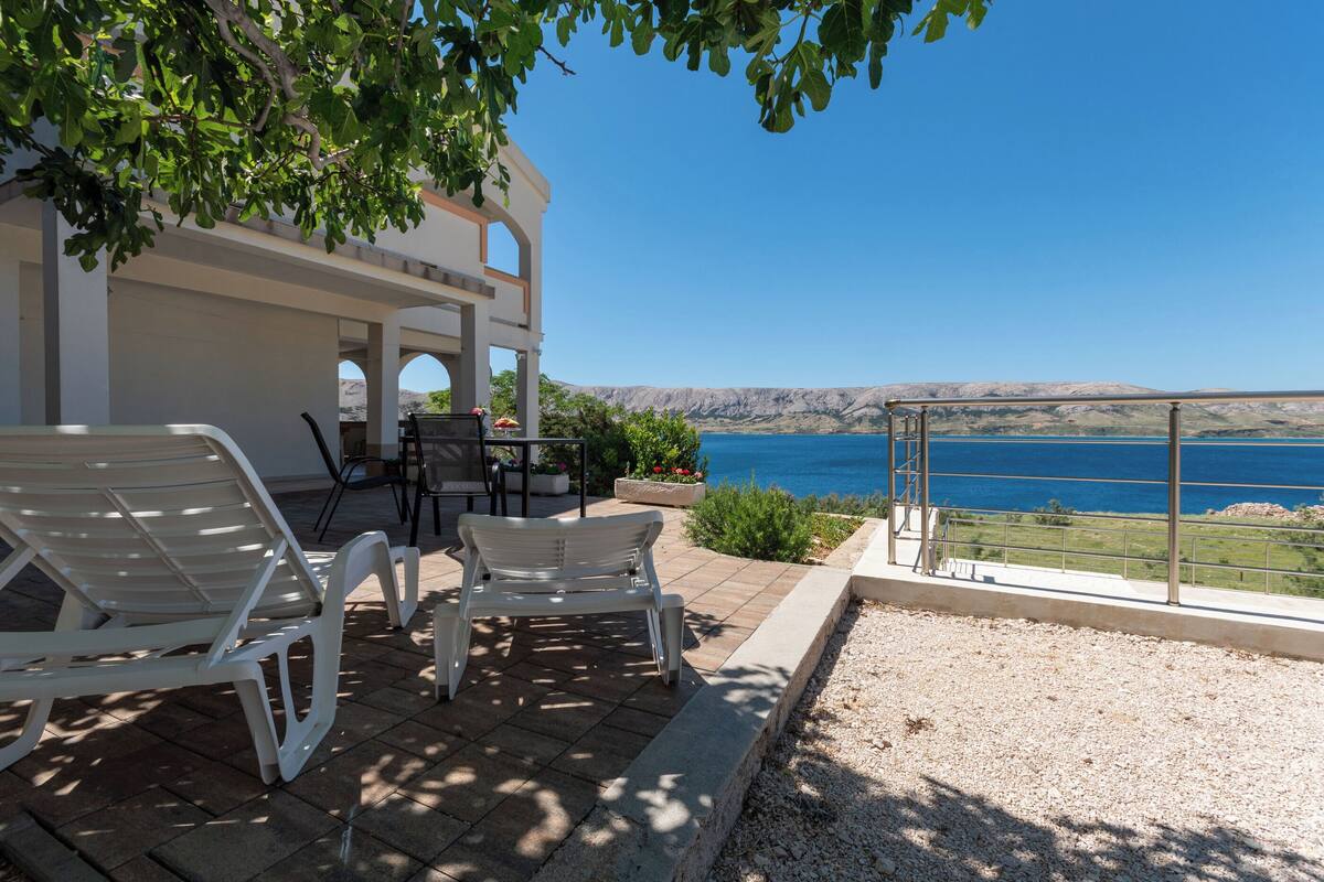 A terrace with white lounge chairs, a table, and a view of the sea.