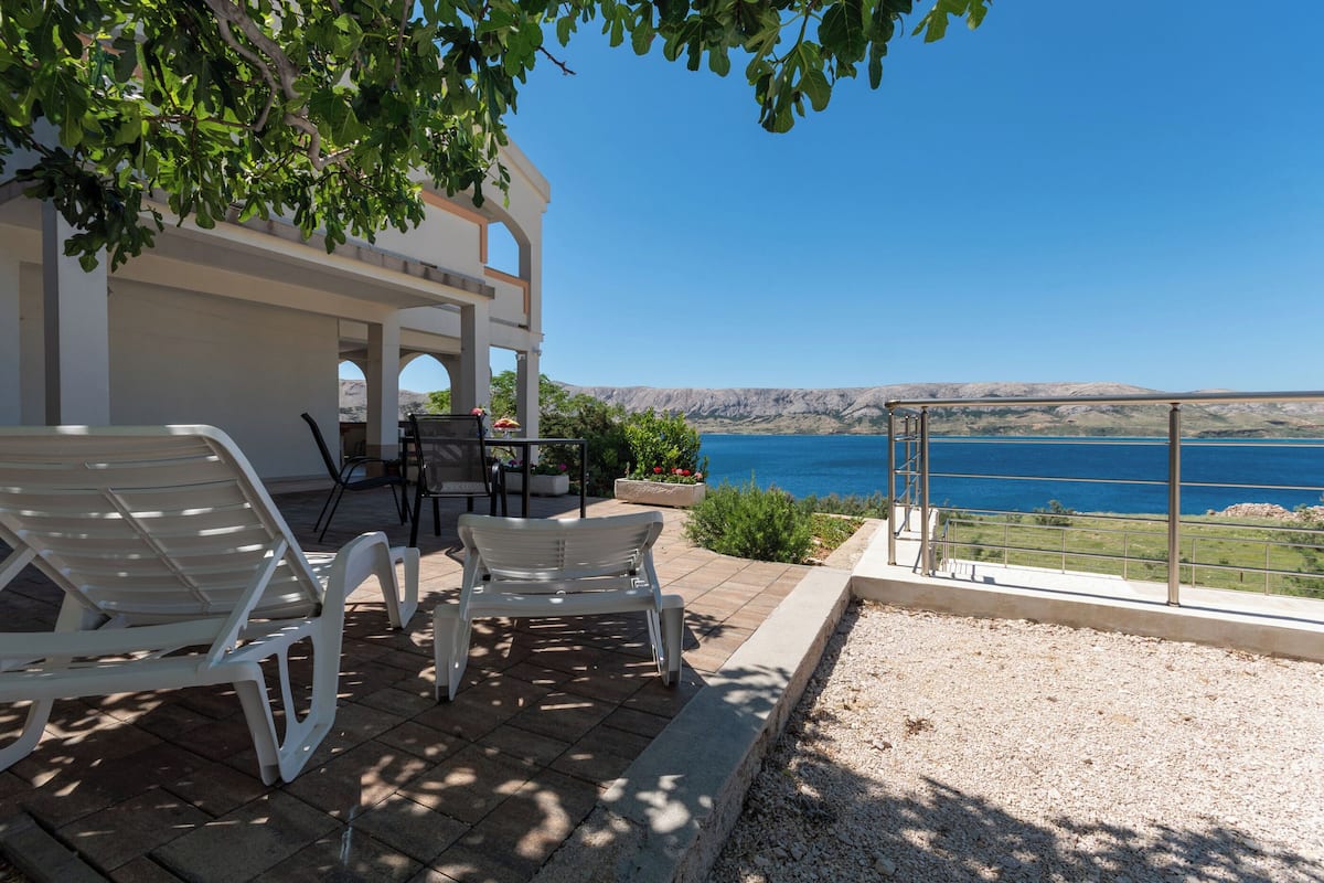 Una terraza con sillones blancos, una mesa y vista al mar.