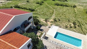 Un edificio con techo de tejas rojas, piscina y vistas a un paisaje verde.