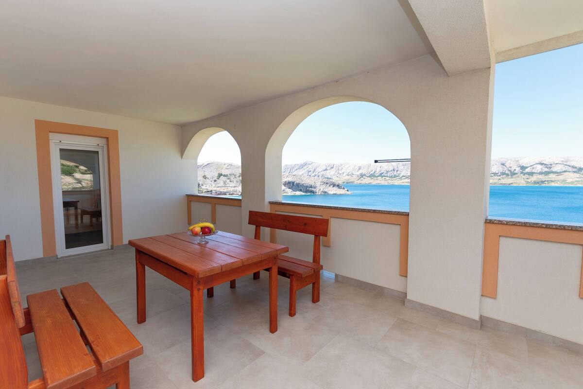 A balcony with a wooden table and chairs, a glass door, and a view of the sea and mountains.