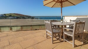 Una terraza con mesa y sillas, una sombrilla y vista al mar.